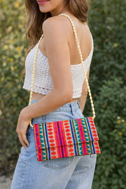 Handwoven boho clutch bag with orange, pink and green ethnic patterns on rustic wooden background